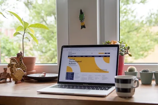 A laptop open on a desk beside a window